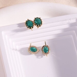 May include: Two pairs of green gemstone earrings with gold settings. The earrings are on a white surface.