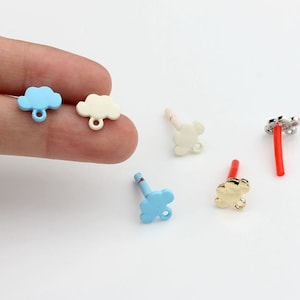 Pode incluir: Conjunto de pequenos pingentes de nuvem de metal em várias cores, incluindo azul, branco e dourado. Os pingentes têm um laço na parte inferior para prender a joias ou outros artesanatos.