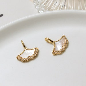 Peut inclure: Deux breloques en forme d'éventail dorées avec des incrustations de nacre blanche et des accents de strass transparents.