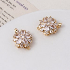 Puede incluir: Dos cierres de color dorado en forma de flor con piedras de circonita cúbica transparentes. Los cierres están diseñados para ser utilizados en la elaboración de joyas.