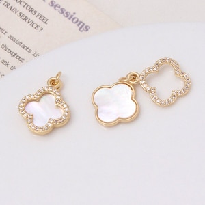 Può includere: Due ciondoli a forma di trifoglio dorati con cristalli trasparenti e un centro in madreperla bianca. Un ciondolo è un trifoglio pieno, l'altro è un trifoglio aperto.