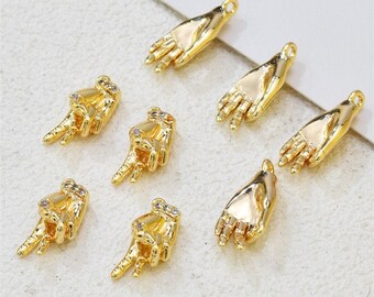 May include: A set of seven gold-tone hand charms with clear rhinestone accents. The charms are in the shape of a hand with the fingers extended, and some of the charms have a peace sign gesture.