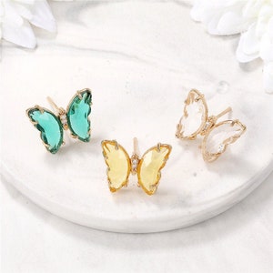 May include: Three pairs of butterfly earrings with crystal accents. The earrings are in green, yellow, and clear.