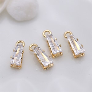May include: Four gold-toned pendant charms with clear rectangular crystal stones. Each charm has a loop at the top for attaching to a necklace or bracelet.