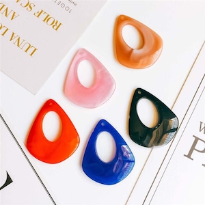 Peut inclure: Cinq ébauches de boucles d'oreilles en plastique de couleurs différentes en forme de larme avec un trou au centre. Les couleurs sont rose, orange, bleu, noir et marron.