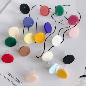 以下が含まれることがあります： 中心に穴が開いたカラフルな丸いイヤリングのブランクの詰め合わせ。ブランクはアクリル製で、赤、青、緑、黄、ピンク、白など、さまざまな色があります。