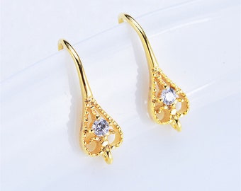 May include: A pair of gold dangle earrings with a delicate, ornate design and a single clear rhinestone in the center of each earring.