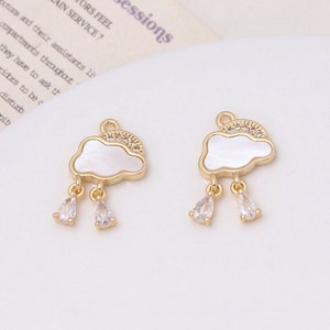 Op de afbeelding: Twee goudkleurige wolkcharms met witte schelpaccenten en heldere kristallen accenten. Elke charme heeft drie hangende kristallen druppels.
