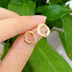 May include: A pair of gold-toned earrings with an irregular, organic shape. Each earring has a small circle cut out in the center.