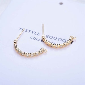 May include: A pair of gold-toned hoop earrings with a row of clear cubic zirconia stones. The earrings have a simple, elegant design.