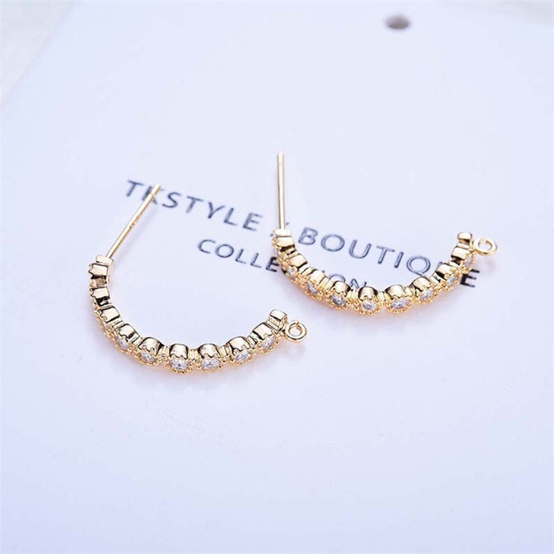 May include: A pair of gold-toned hoop earrings with a row of clear cubic zirconia stones. The earrings have a simple, elegant design.