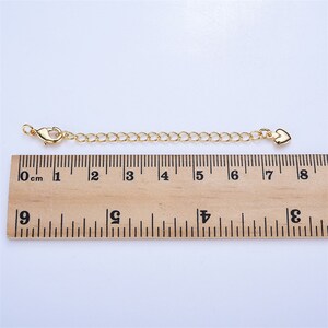 May include: A gold chain extender with a lobster clasp on one end and a heart charm on the other. The extender measures 7 cm in length.