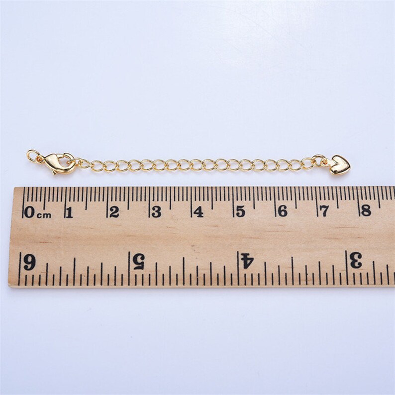 May include: A gold chain extender with a lobster clasp on one end and a heart charm on the other. The extender measures 7 cm in length.