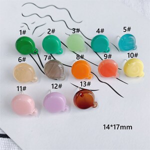Pode incluir: Treze pingentes de chaton de resina de diferentes cores em forma de bolha de diálogo. Os pingentes estão dispostos em três filas sobre uma superfície branca. Os pingentes medem aproximadamente 1,4 cm por 1,7 cm.