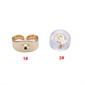May include: Two earring backs are shown. One is gold-colored, with a butterfly shape and a central hole. The other is a clear, rounded earring back with a gold-colored metal insert. The numbers 1# and 2# are printed below each earring back.