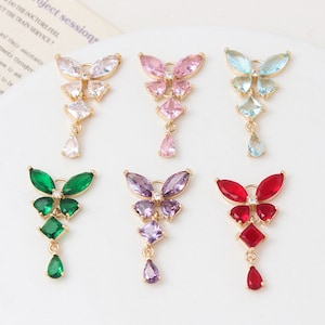 May include: Six gold butterfly charms with dangling crystal drops. The butterflies are in different colours: white, pink, light blue, green, purple, and red.