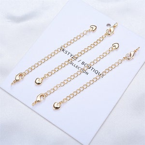 May include: Four gold-toned chain extenders with heart-shaped charms and lobster claw clasps. Each extender is approximately 2 inches long.
