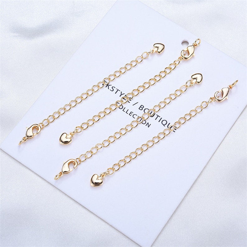 May include: Four gold-toned chain extenders with heart-shaped charms and lobster claw clasps. Each extender is approximately 2 inches long.