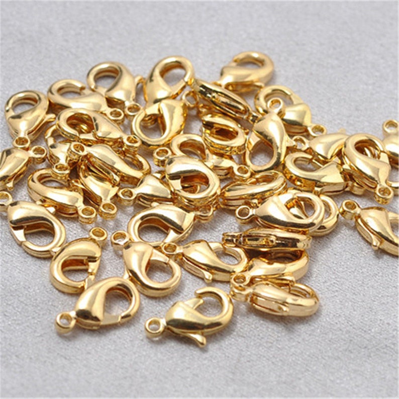 May include: A pile of gold-toned metal lobster claw clasps. These clasps are commonly used for jewelry making and crafting.