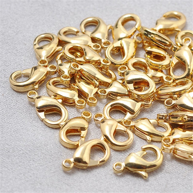 May include: A pile of gold-toned metal lobster claw clasps. These clasps are commonly used for jewelry making and crafting.