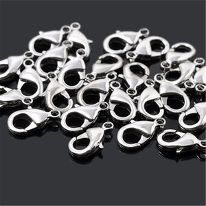 May include: A pile of silver-toned lobster clasps, a type of fastener used for jewelry making.