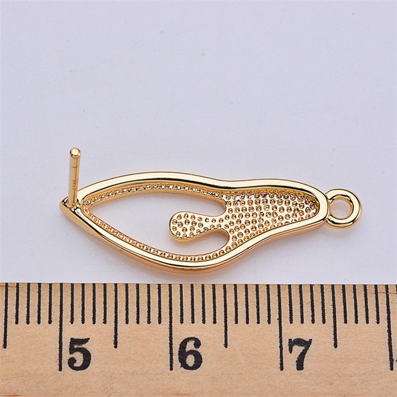 May include: Gold-tone metal earring finding with a decorative, openwork design. The finding measures approximately 1.75 inches in length.