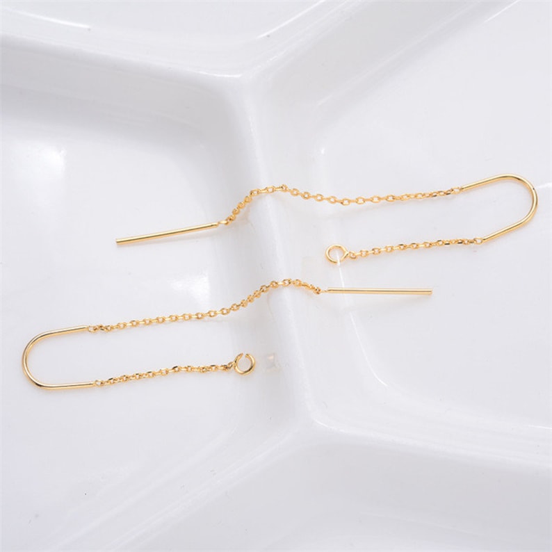 May include: A pair of gold chain earrings with a small bar hanging from each chain.