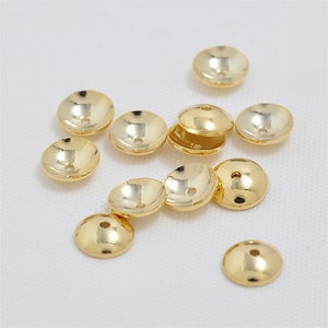 May include: A group of 12 gold-colored metal bead caps with a small hole in the center. The caps are round and have a slightly domed shape.