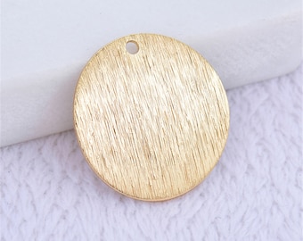 May include: Gold-toned round metal pendant with a brushed finish and a small hole at the top for attaching a chain or cord.