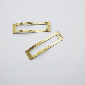 May include: Two gold-toned metal rectangular frames with a curved shape. The frames have a hole at the top.