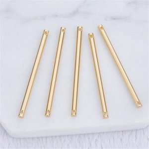 May include: Five gold metal rods with a small hole at each end. The rods are arranged in a fan shape on a white surface.