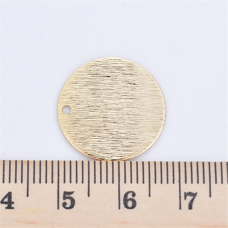 以下が含まれることがあります： 表面がテクスチャ加工された金色の金属製の円形で、上部に小さな穴があります。円の直径は約3.8cmです。