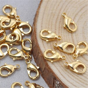 May include: A close-up of a group of gold-toned lobster claw clasps. The clasps are arranged on a wooden surface.