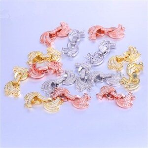 May include: Assortment of 12 gold, silver, and rose gold tone metal connector charms with clear cubic zirconia stones. Each charm features a double-loop design with a curved shape.