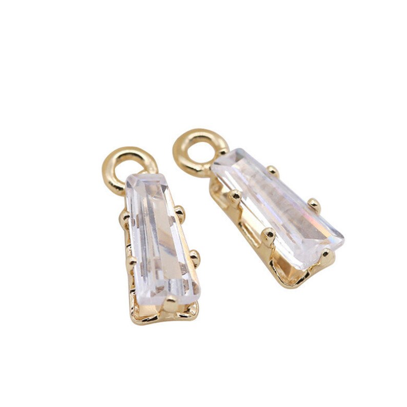 May include: Two gold-tone pendant charms with clear crystal stones. Each charm has a loop at the top for attaching to a necklace or bracelet.