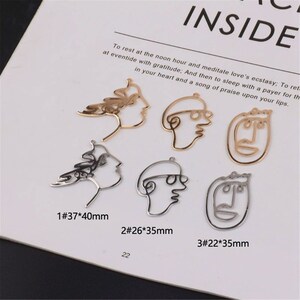May include: Six gold and silver metal charms in the shape of abstract faces. The charms are approximately 3.7 cm, 2.6 cm, and 2.2 cm in size. The charms are labeled with numbers and measurements.