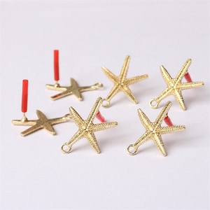 May include: Five gold-colored starfish charms with red jump rings. The charms are perfect for jewelry making or crafting.