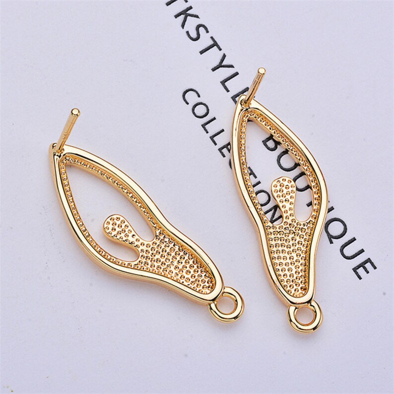 May include: Two gold-tone earring findings with a cutout design of a person. The findings have a loop at the bottom for attaching a dangle.