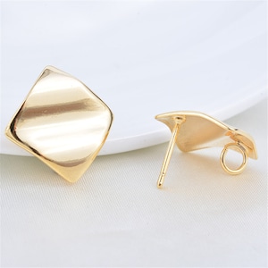 May include: A pair of gold-toned earring findings with a square-shaped design. The findings have a post and a loop for attaching a charm or pendant.