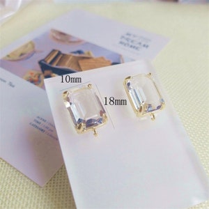 May include: Two clear glass rectangular earring blanks with gold-toned metal settings and jump rings. The blanks measure 18mm by 10mm.