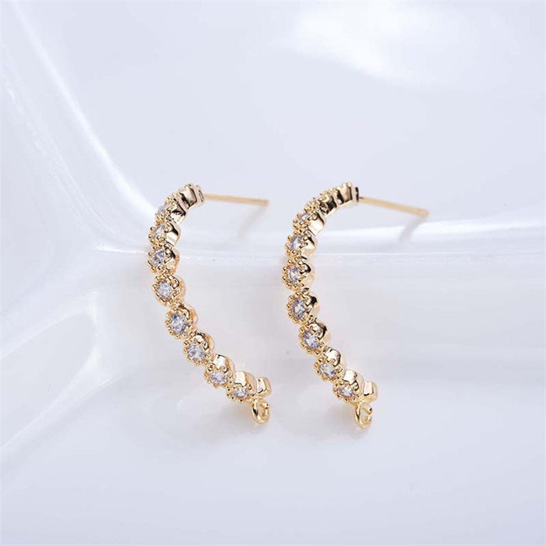 May include: A pair of gold hoop earrings with a row of clear cubic zirconia stones around the hoop.