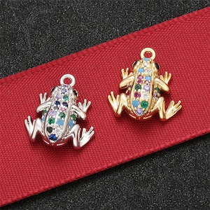 May include: Two frog charms with colorful rhinestones. One charm is gold and the other is silver.