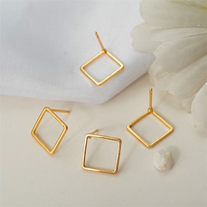 Op de afbeelding: Drie gouden vierkante oorbelblanken met pinnen. De oorbelblanken liggen op een wit oppervlak.