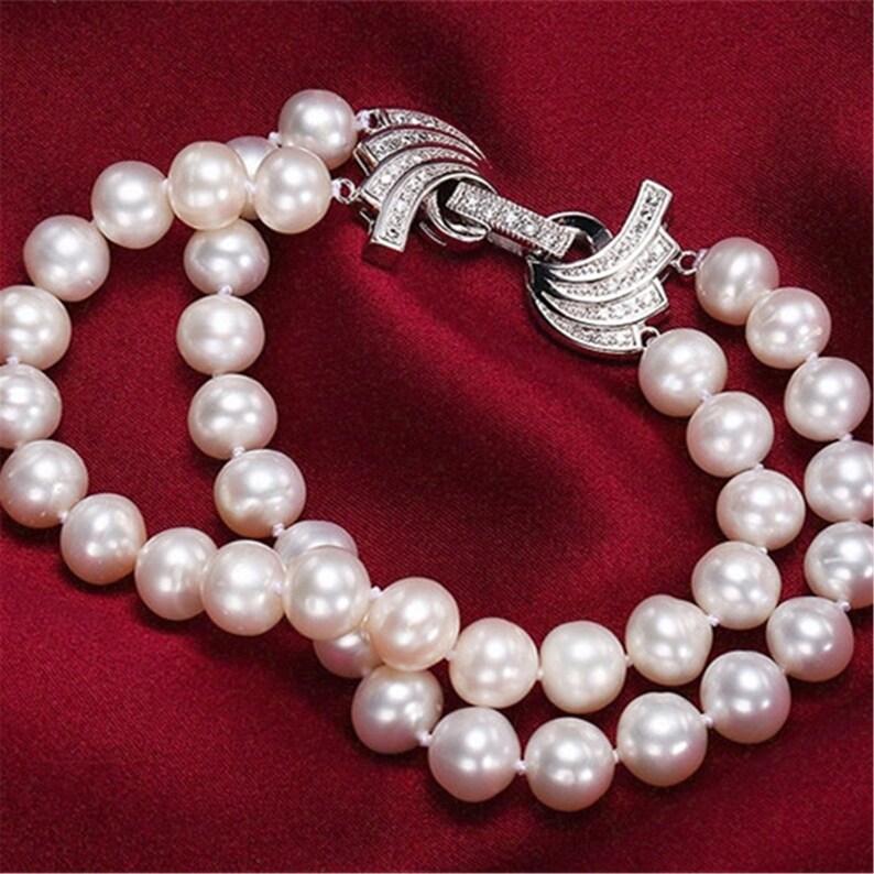 May include: A double strand pearl bracelet with a silver clasp adorned with clear cubic zirconia stones. The pearls are white and round.
