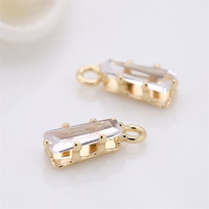 May include: Two gold-tone charms with clear rectangular crystal accents. The charms have a small loop at the top for attaching to jewelry.