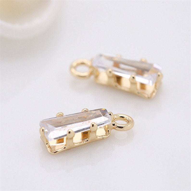 May include: Two gold-tone charms with clear rectangular crystal accents. The charms have a small loop at the top for attaching to jewelry.