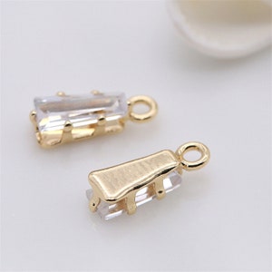 May include: Two gold-tone pendant charms with clear rectangular crystal stones. The charms have a loop at the top for attaching to a necklace or bracelet.