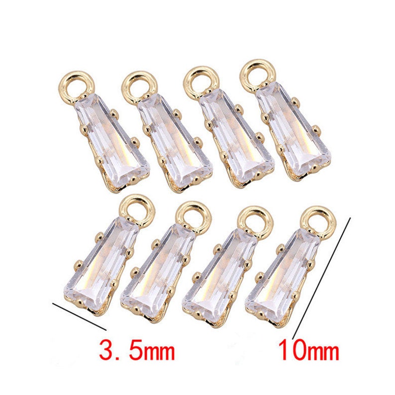 May include: Eight gold-toned pendant charms with clear rectangular crystal stones. The charms are 3.5 mm wide and 10 mm long.