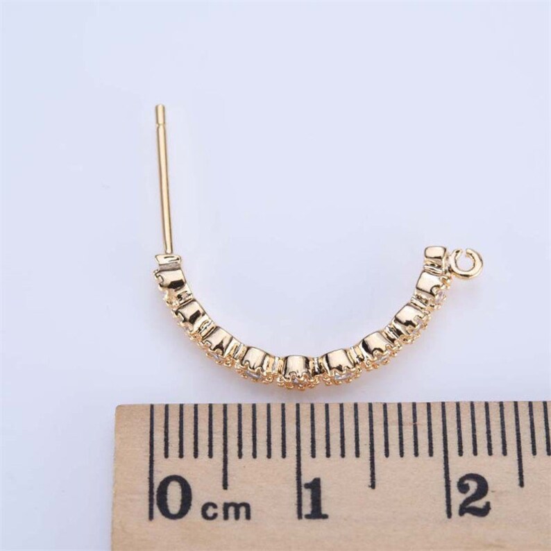 May include: Gold hoop earrings with clear cubic zirconia stones. The earrings are approximately 1 cm in diameter.