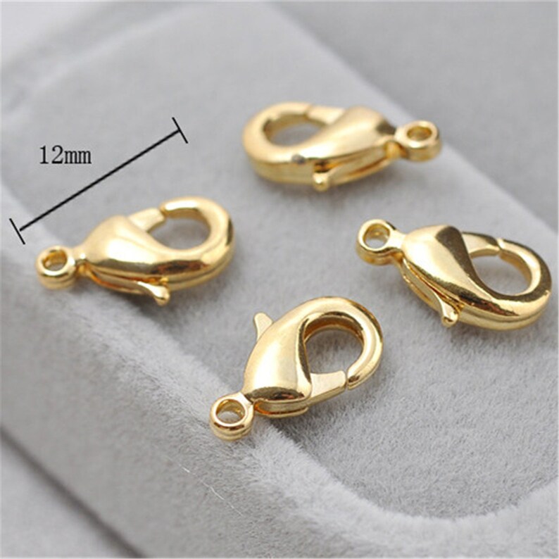 May include: Four gold-toned metal lobster claw clasps, each measuring 12 mm in length. These clasps are commonly used for jewelry making and crafting.